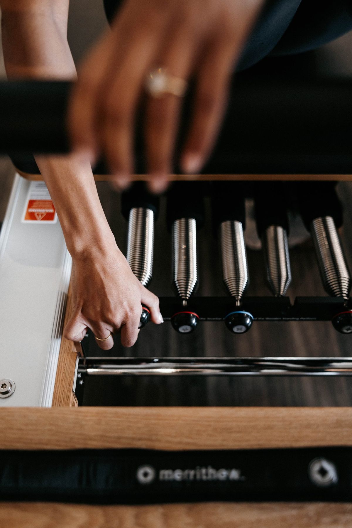 Hands adjusting a Merrithew reformer, the locked spec that produces the Method's calibration.