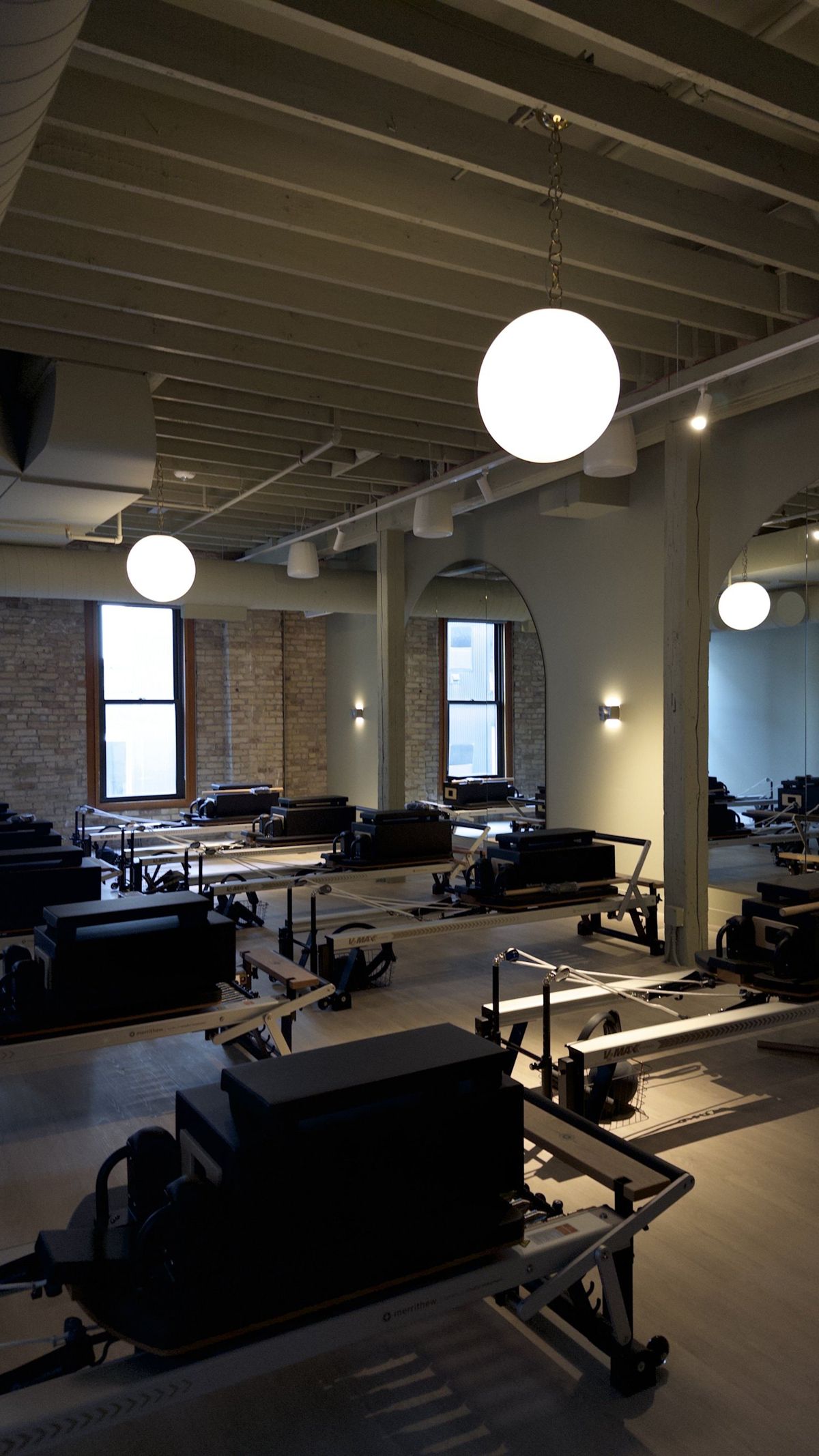 A quiet, empty Rêve studio: reformers, brick, and globe lights before the room fills.