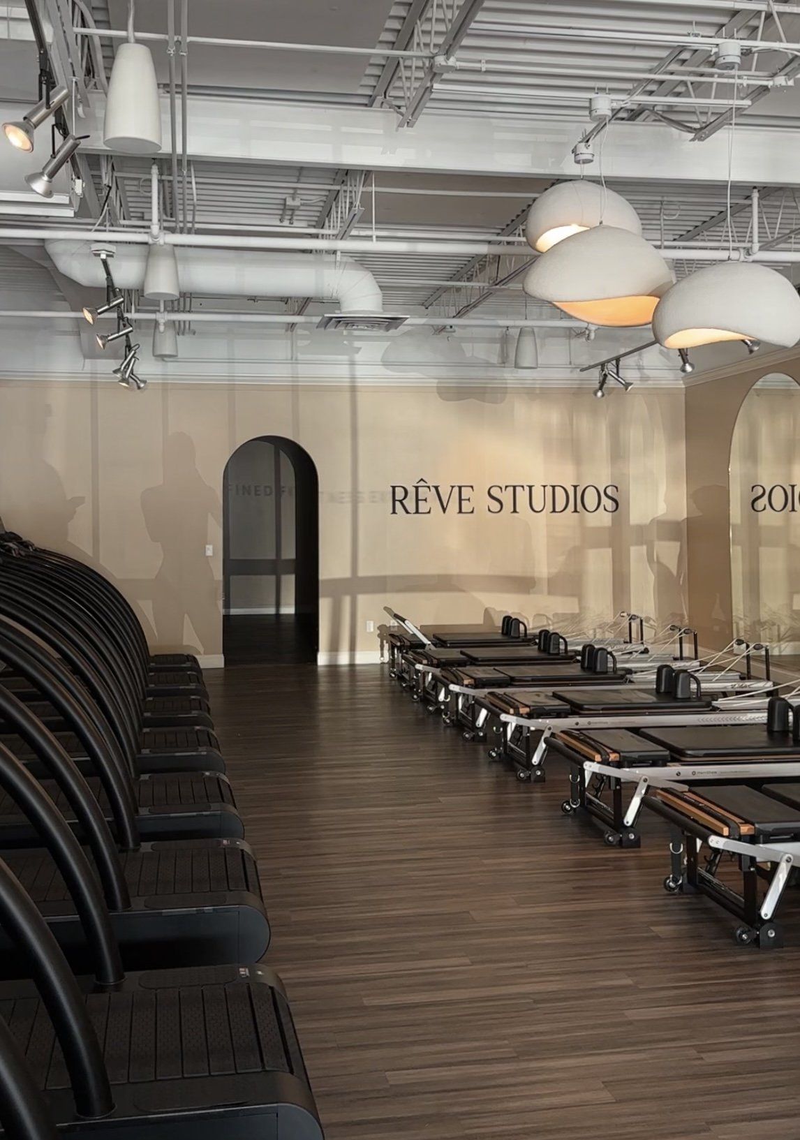 An empty Rêve studio before class. Reformers, brick, and the RÊVE STUDIOS wall signage: the system before the people.